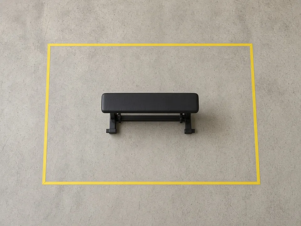 Top-down view of a garage floor where a taped rectangle marks an even clearance zone around a flat bench.